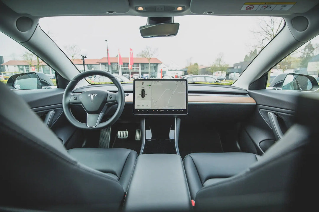Black leather-trimmed tesla model 3 interior with a central touchscreen display and minimalist dashboard design.