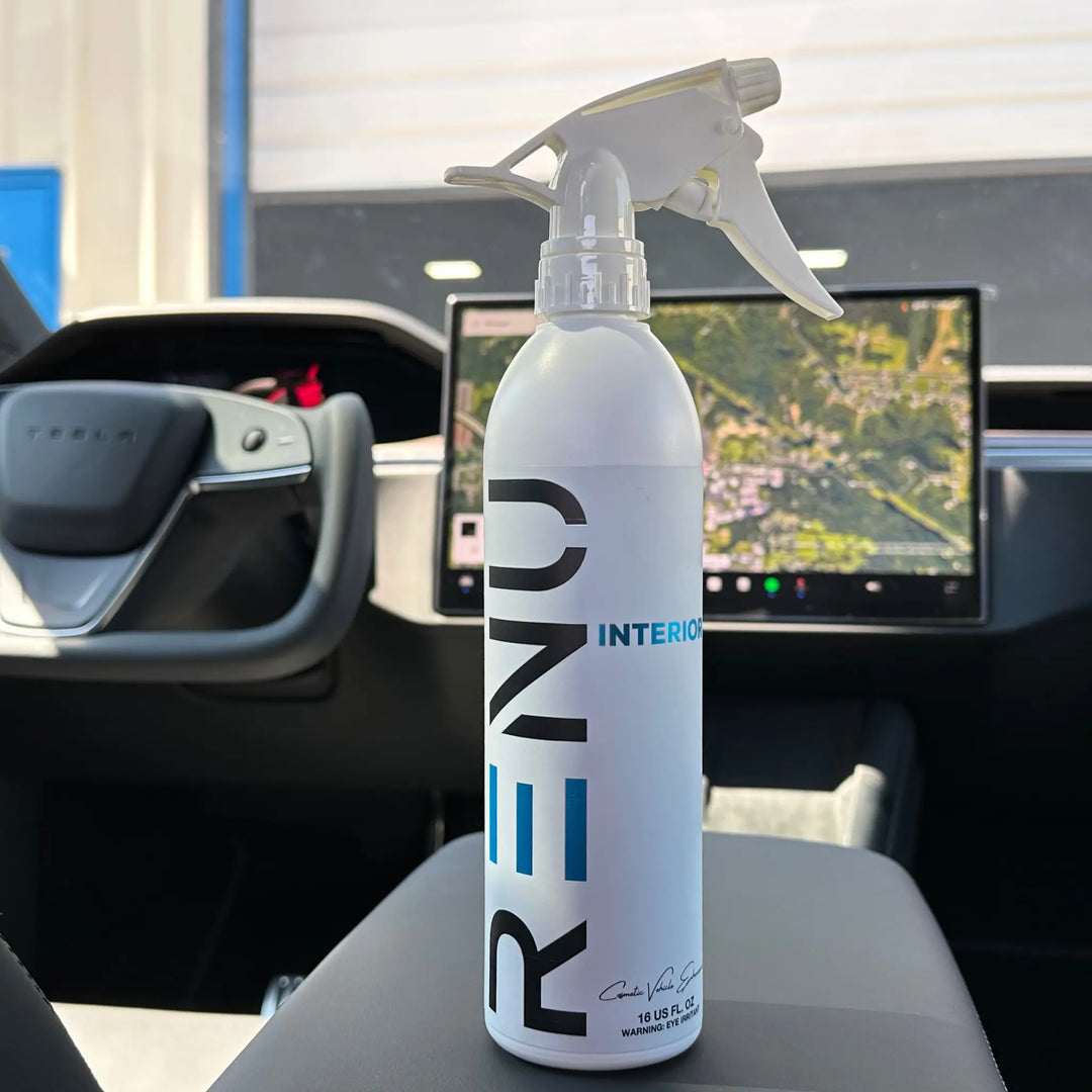 Spray bottle labeled INTERIOR placed inside a modern car near the steering wheel and dashboard screen.