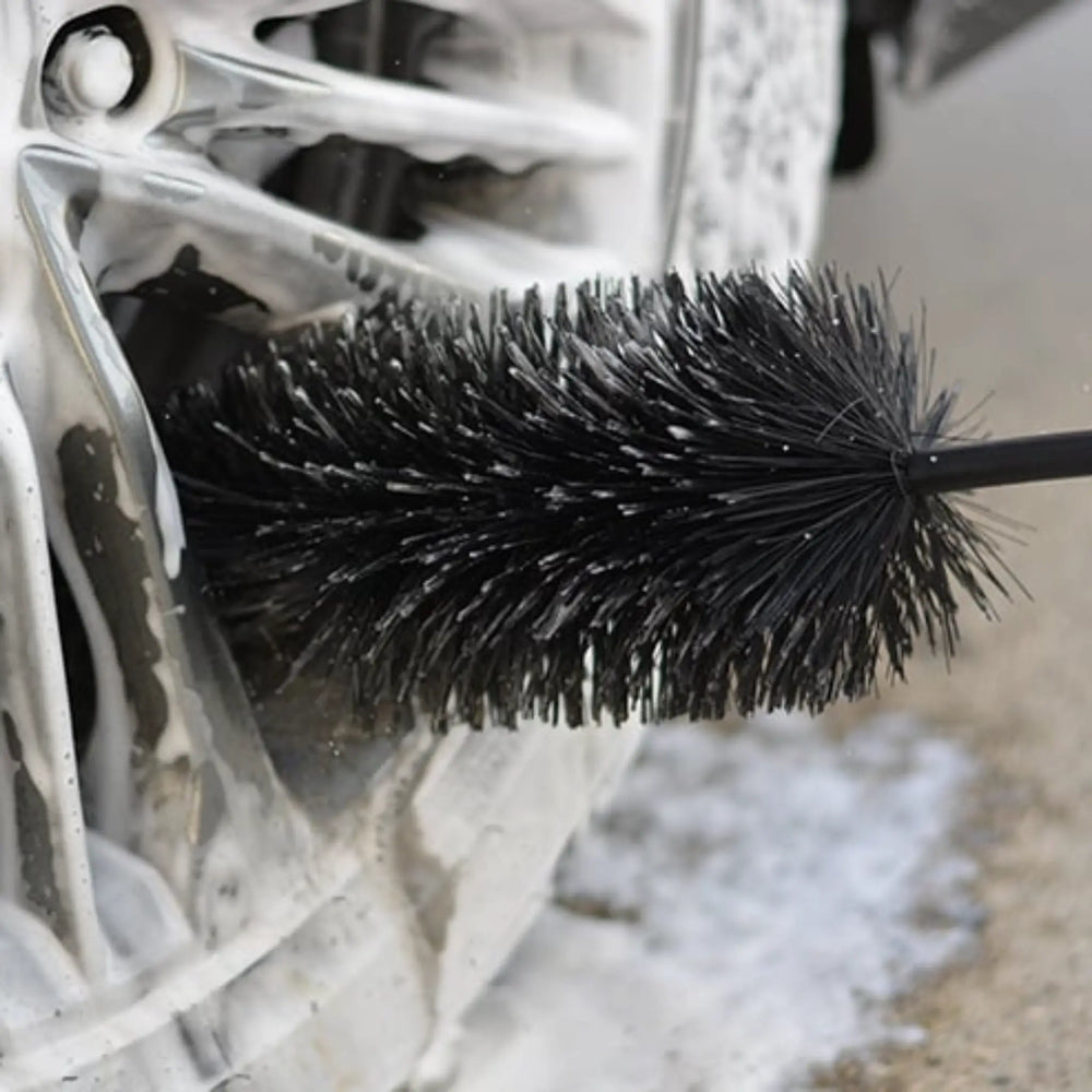 Spoke & Wheel Barrel Brush cleaning foam from inside a car wheel rim with black bristles on a long handle.