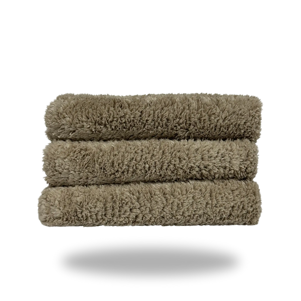 Stack of three soft tan 600 edgeless microfiber towels neatly folded against a white background