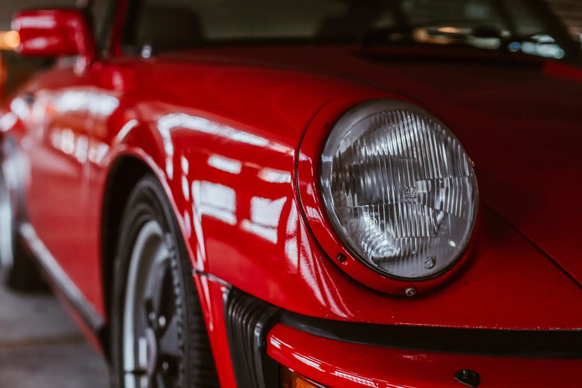 Vibrant red porsche sports car headlight with chrome bezel and classic round design.